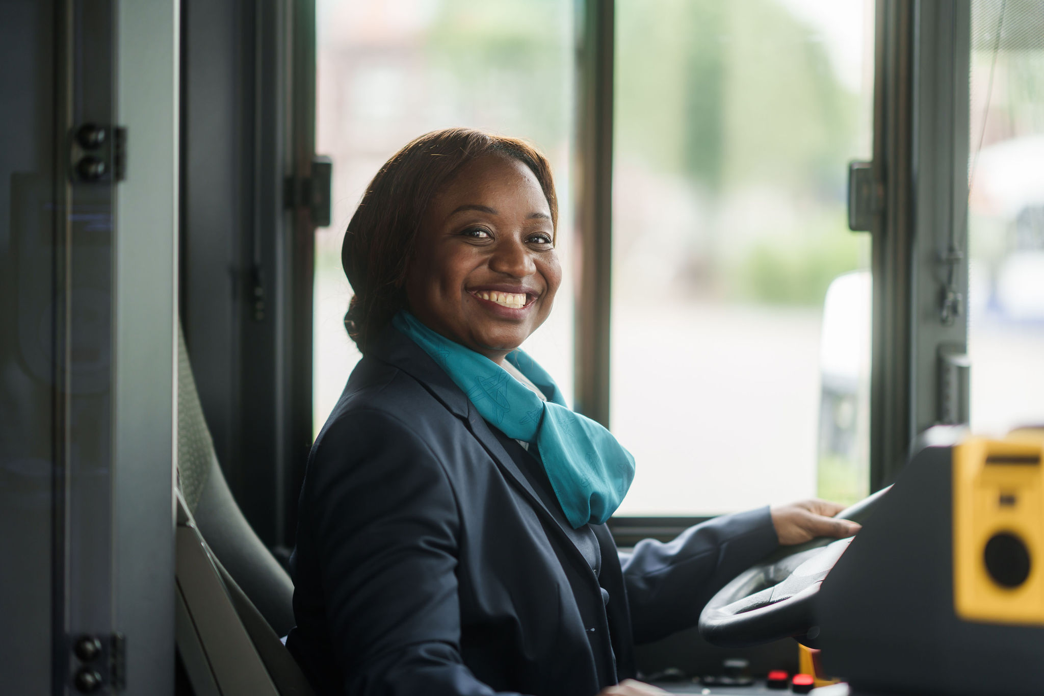 Een buschauffeur in haar Arriva-uniform zit achter het stuur en kijkt lachend opzij.